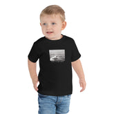 Toddler wearing a black surf graphic tee with sentence "Right at Your Heels" under graphic.